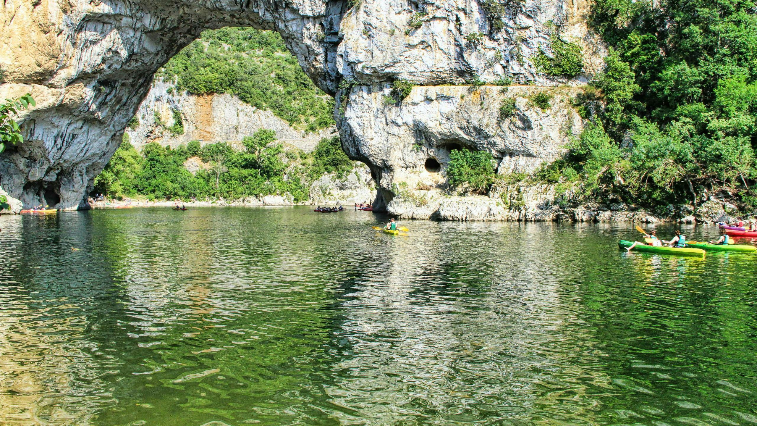Eine Gruppe an Leuten paddelt beim Kanufahren in Ardèche durch die Pont-D'Arc.