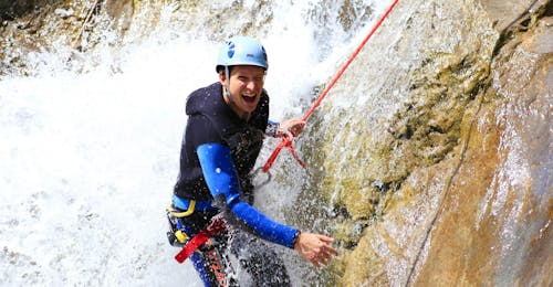 Ein Teilnehmer des Canyoning in der Hochalpschlucht mit Fun Rafting Lechtal seilt sich über einen tosenden Wasserfall in der Schlucht ab.
