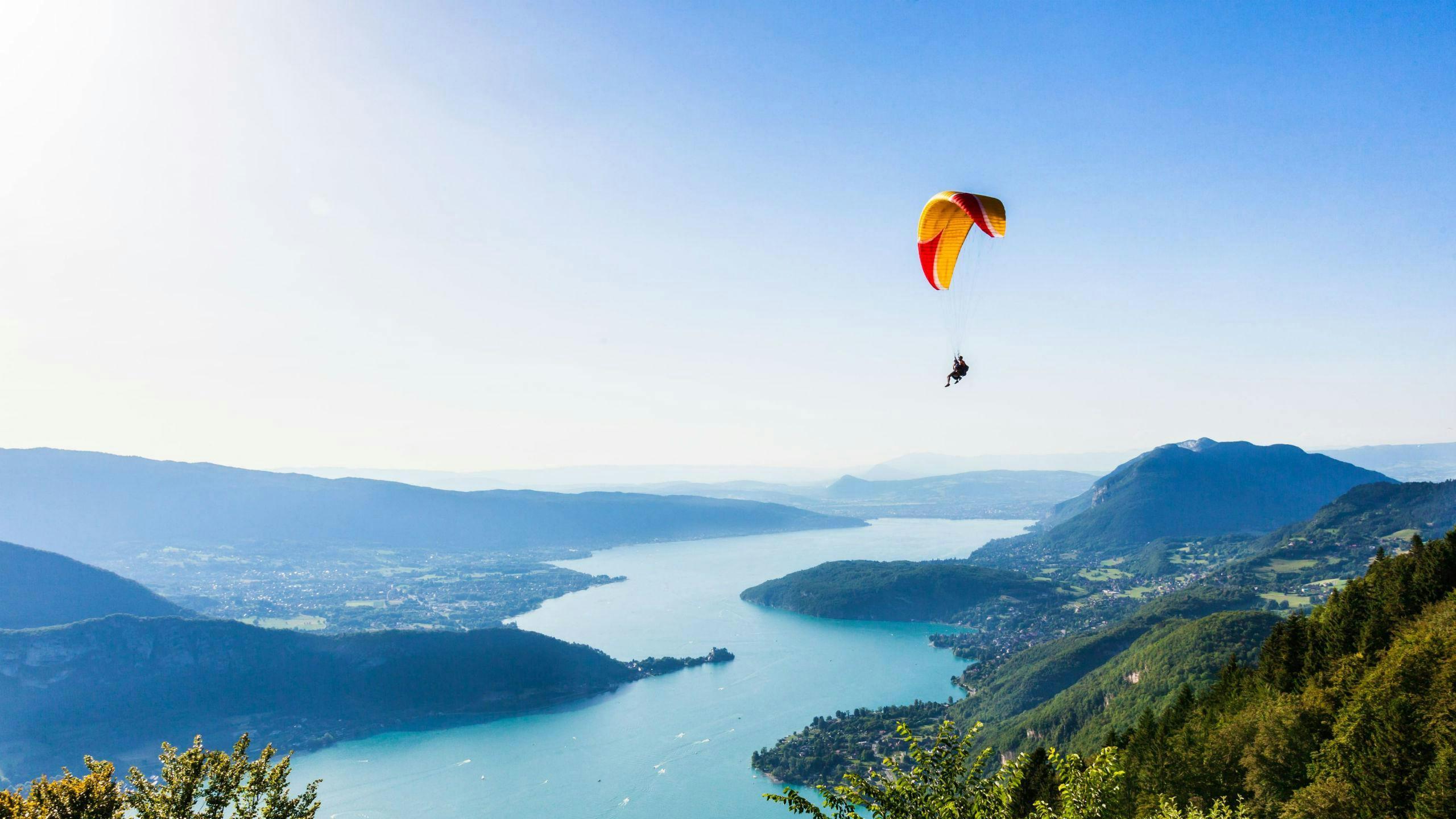 A tandem master and their passenger are gently gliding through the skies while paragliding at Lac d'Annecy.
