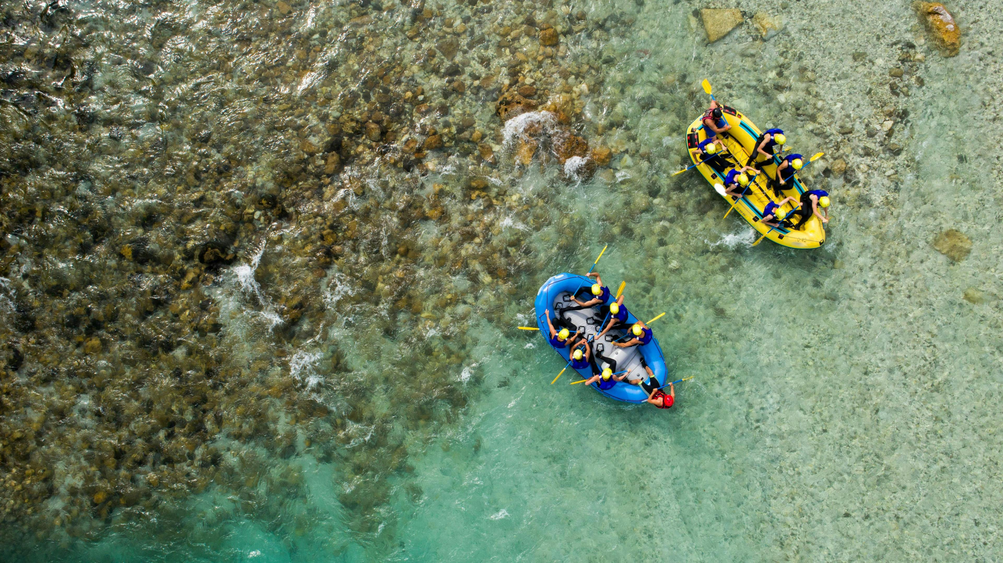 Two groups of people are paddling across the Soca River while rafting near Bled.