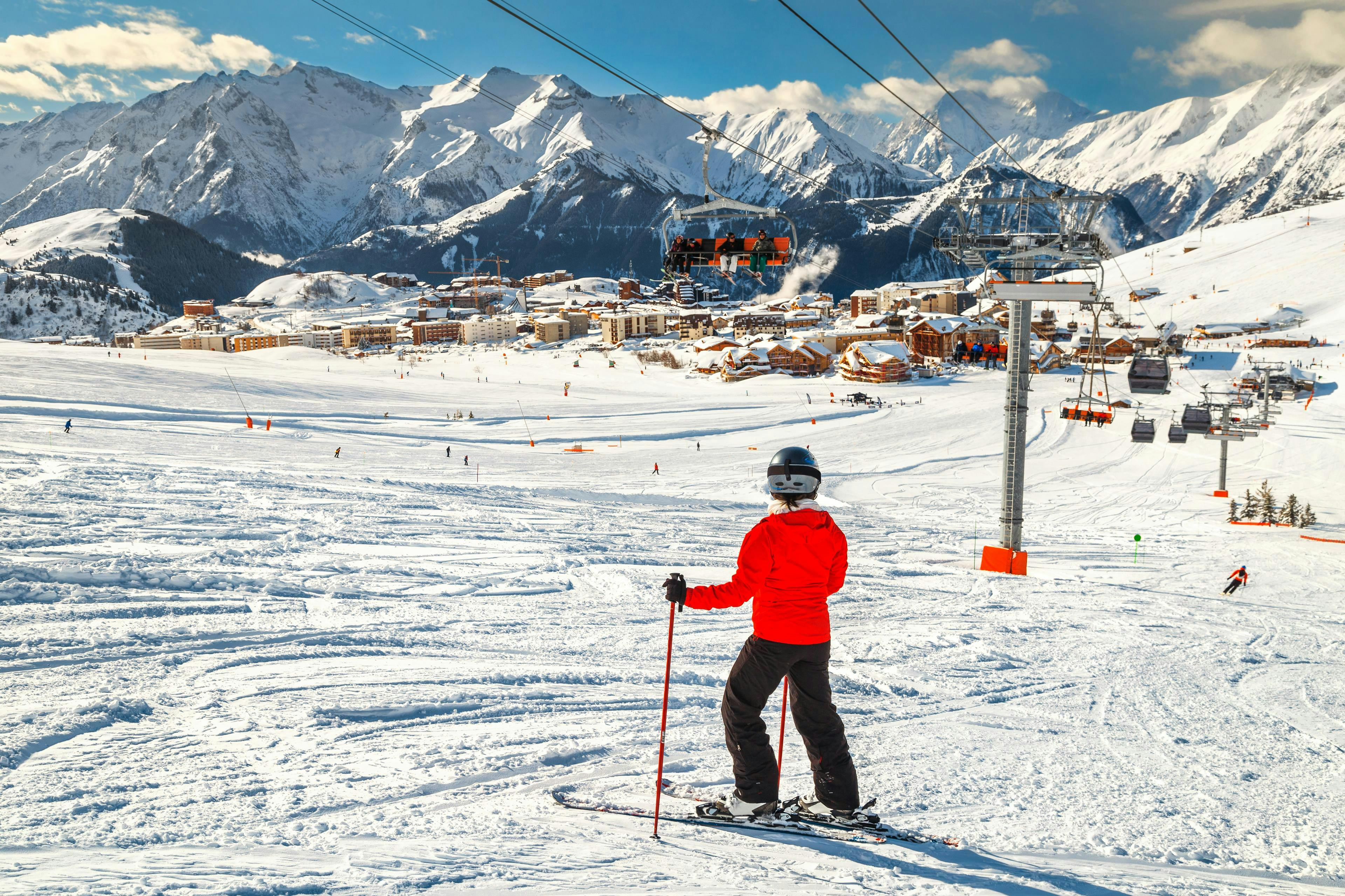 Un skieur fait une pause pendant son cours de ski pour profiter de la vue sur la station de l'Alpe d'Huez depuis les pistes.