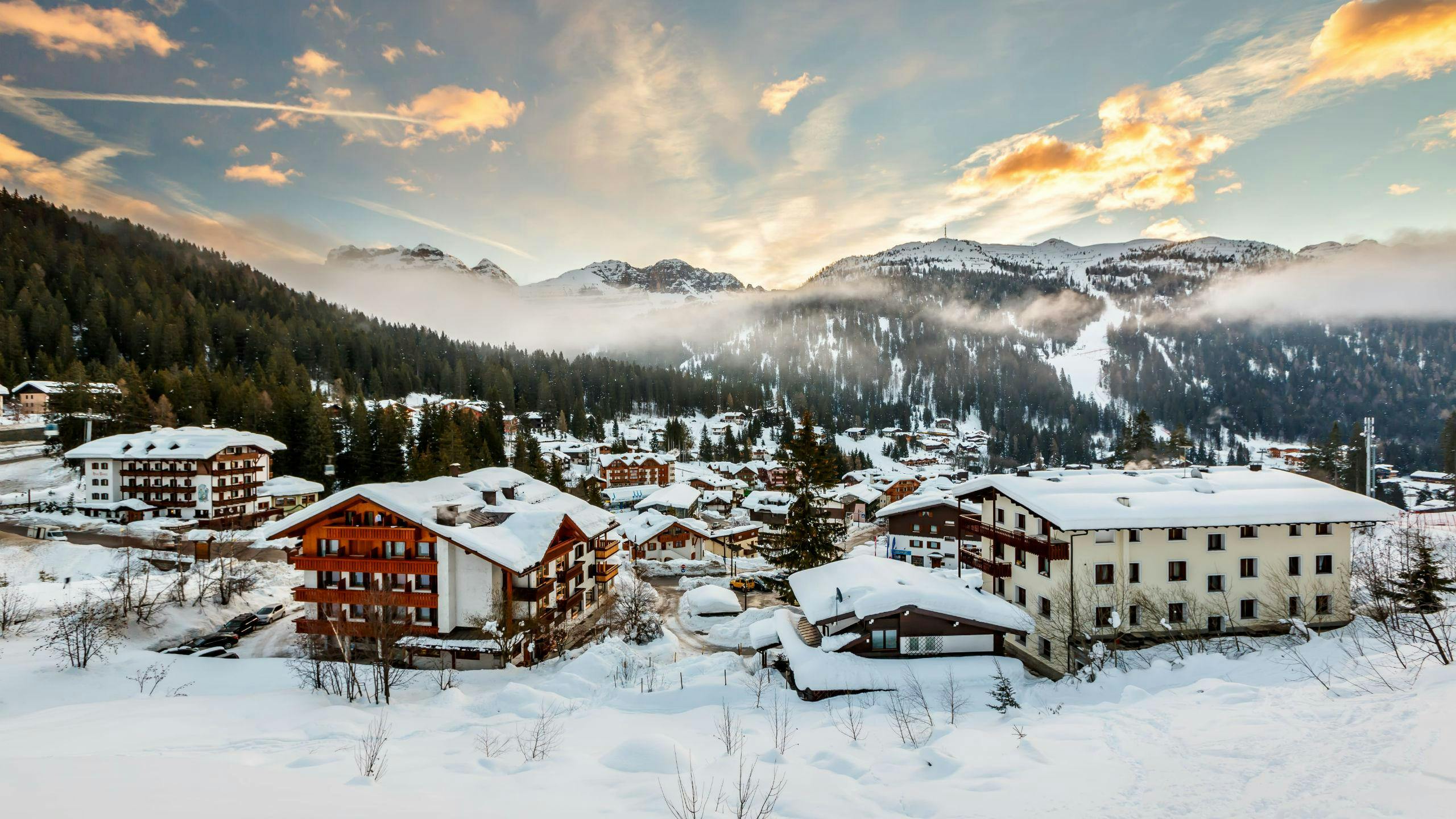 Immagine del sole che tramonta dietro le montagne nel comprensorio sciistico italiano di Madonna di Campiglio, dove i visitatori possono imparare a sciare durante le lezioni di sci impartite dalle scuole sci locali.
