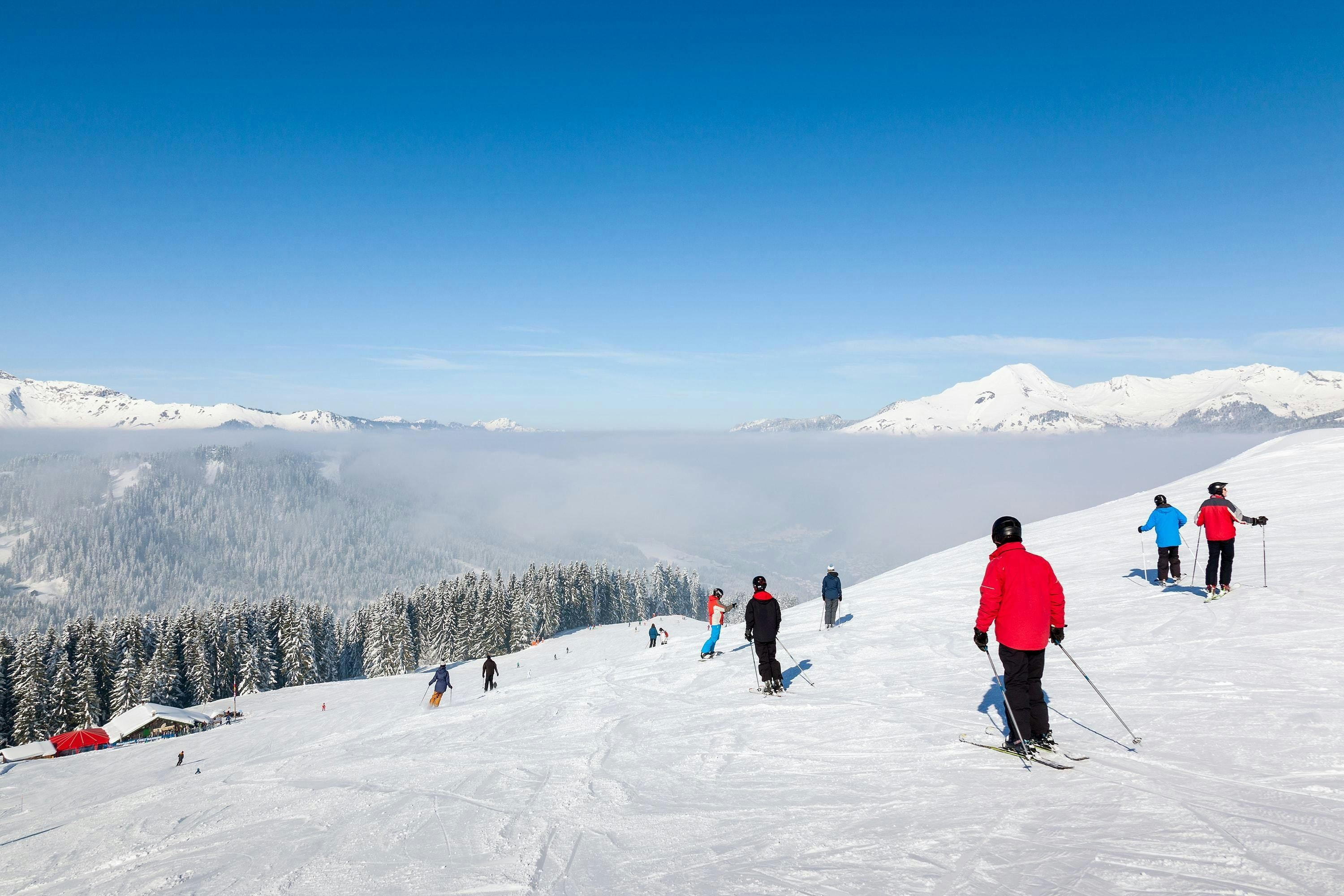 A number of skiers is skiing down a ski slope in the ski resort of Morzine, with a beautiful view of the surrounding mountainscape that is visible to all who book ski lessons with the local ski schools. 